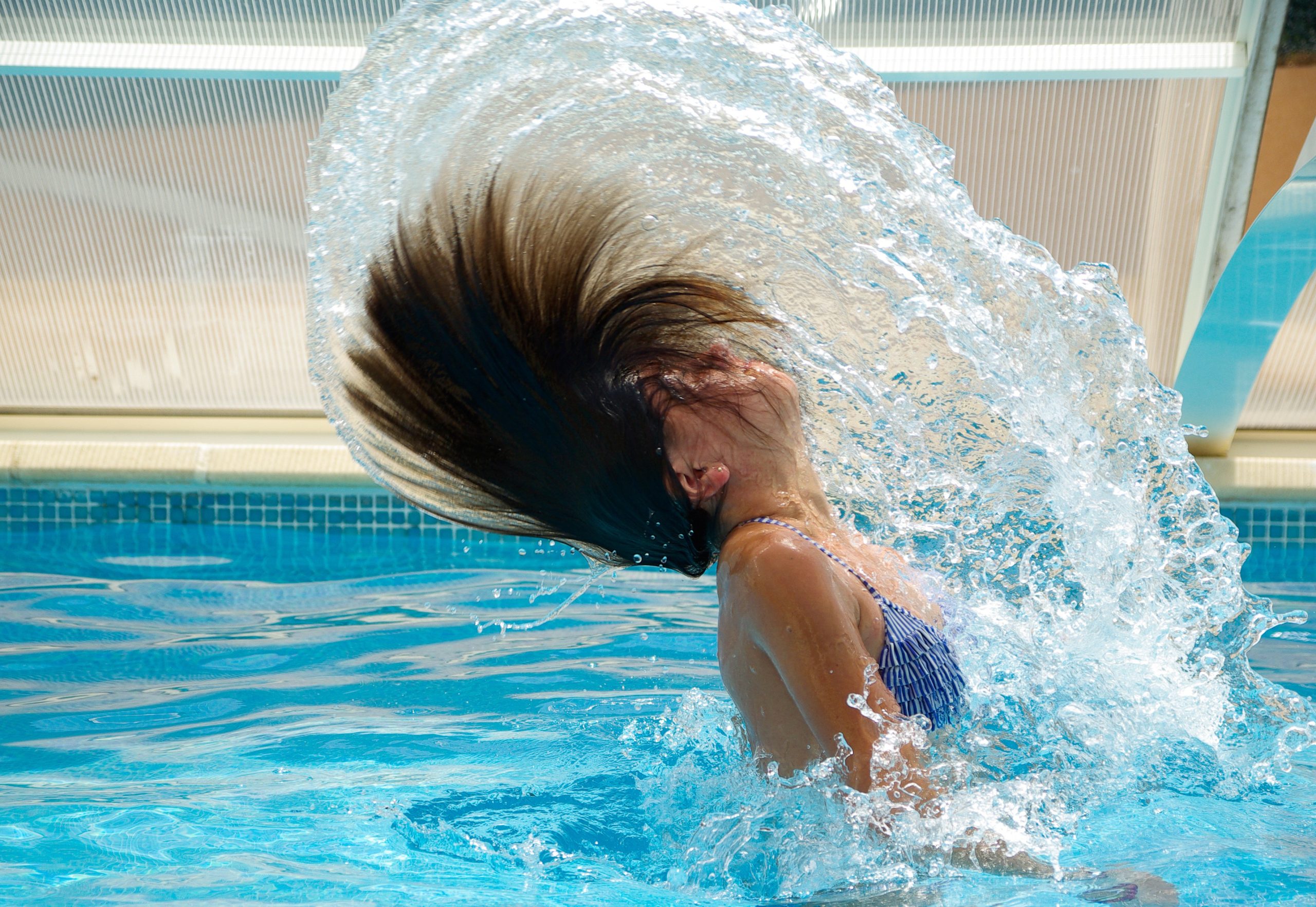 Donna in piscina che muove i capelli nell'acqua.